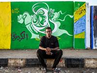 Sudanese graffiti artist Belal Abdelrahaman sits in front of a recently painted mural made by his team during a protest near the army headquarters in the capital Khartoum  OZAN KOSE / AFP