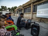 A member of Syrian-Kurdish filmmaker Shero Hinde's mobile cinema "Komina Film" initiative prepares a laptop connected to a projector and screen for a film screening for children at a school yard in the village of Shaghir Bazar, 55 kilometres southest of Qamishli in the Kurdish-populated areas of northeastern Syria's Hasakeh province, on July 28, 2019. DELIL SOULEIMAN / AFP