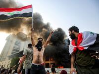 A topless masked protester flashes the victory gesture as he waves an Iraqi national flag before a burning building during a demonstration against state corruption and poor services, between the capital Baghdad's Tahrir Square and the high-security Green Zone district, on October 1, 2019.  AHMAD AL-RUBAYE / AFP