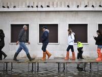 People walk on a footbridge across a flooded street after an exceptional overnight "Alta Acqua" high tide water level, on November 13, 2019 in Venice. Venice was hit by the highest tide in more than 50 years late November 12, with tourists wading through flooded streets to seek shelter as a fierce wind whipped up waves in St. Mark's Square. Marco Bertorello / AFP