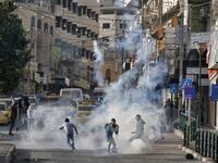 Palestinian youths run from tear gas smoke fired by Israeli security forces on November 26, 2019 during clashes in the West Bank city of Hebron during a Palestinian "day of rage" against a recent US decision to no longer consider settlements in the West Bank illegal. A Palestinian convicted over the killing of three Israelis died of cancer in custody today, officials said. The death, which sparked Palestinian accusations of neglect, comes amid heightened tension with protests already scheduled in multiple p