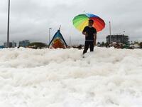 A man holds an umbrella over foamy discharge, caused by pollutants, as it mixes with the surf at Marina beach in Chennai on December 1, 2019. Arun SANKAR / AFP