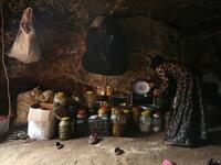 A woman holds a plate and a saucepan as she stands by food stores including pickled olives inside an underground shelter where several families of internally displaced Syrians from Aleppo and Idlib provinces are taking refuge, in the village of Taltunah about 15 kilometres northwest of Idlib in the northwestern Idlib province, on February 23, 2020. Aref TAMMAWI / AFP