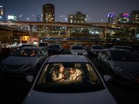 In a photo taken on March 21, 2020 a couple look at a mobile phone as they sit in a car at a screening at a drive-through cinema in Seoul. Box office numbers in South Korea -- which has 8,897 confirmed virus cases -- have plummeted in recent weeks due to the epidemic, with authorities urging the public to avoid large crowds. But at drive-in cinemas, moviegoers can enjoy a movie from the comfort of their cars, parked in front of a large outdoor screen.  Ed JONES / AFP