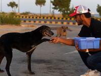 This photo taken on April 2, 2020 shows resident Ali Khurshid playing with stray dogs before feeding them on a street near Clifton beach during a government-imposed nationwide lockdown as a preventive measure against the COVID-19 coronavirus, in Karachi. Abandoned when Pakistan's largest cities went into lockdown, hundreds of caged cats, dogs and rabbits have been found dead inside pet markets hurriedly shuttered as the coronavirus spread. Animals still alive in the corner of Karachi's sprawling Empress Mar