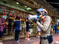 A police officer enforces social distancing as people wearing face masks amid fears of the spread of COVID-19 coronavirus line up to sell their jewelries in front of a gold shop in Bangkok's Chinatown on April 15, 2020. Hundreds of Bangkok residents rushed to goldsmith shops in order to sell their jewelries as gold prices reached its highest levels since 2012. Mladen ANTONOV / AFP