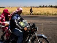 A family rider a motorcycle past a Kurdish female volunteer, from the newly formed Community Protection Forces, as she patrols a wheat field, against threats by jihadists to burn the crops, during harvest season on June 13, 2020, in the countryside east of Qamishli in Syria's northeastern Hasakah province. Delil SOULEIMAN / AFP