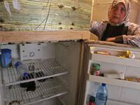 Holding her fridge door open, Fadwa Merhebi explains she already downsized once because she could not afford enough food to fill it up. Now it contains only a bottle of mineral water and two cucumbers. | A Lebanese woman displays the content of her refrigerator. Image Credit: AFP