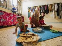 A woman feeds a child while sitting on the floor at a former classroom in a school building where Syrians -- displaced from the area of Ras al-Ain by the Turkish offensive on the northeast -- are staying in the city of Hasakah, on June 30, 2020. Delil SOULEIMAN / AFP