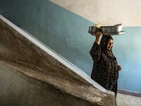 A woman walks down a stairwell while carrying pots on her head at a school building where Syrians -- displaced from the area of Ras al-Ain by the Turkish offensive on the northeast -- are staying in the city of Hasakah, on June 30, 2020. Delil SOULEIMAN / AFP