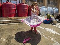 A girl walks past women washing pots and pans by cisterns at the yard of a school building where Syrians -- displaced from the area of Ras al-Ain by the Turkish offensive on the northeast -- are staying in the city of Hasakah, on June 30, 2020. Delil SOULEIMAN / AFP