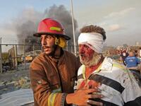 A wounded man is helped by a fireman near the scene of an explosion in Beirut on August 4, 2020. Two huge explosion rocked the Lebanese capital Beirut, wounding dozens of people, shaking buildings and sending huge plumes of smoke billowing into the sky. Lebanese media carried images of people trapped under rubble, some bloodied, after the massive explosions, the cause of which was not immediately known.  ANWAR AMRO / AFP
