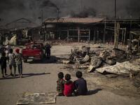 Children sit on the ground in the burnt camp of Moria on the island of Lesbos after a major fire broke out, on September 9, 2020. Thousands of asylum seekers on the Greek island of Lesbos fled for their lives on September 9, 2020 as a huge fire ripped through the camp of Moria, the country's largest and most notorious migrant facility. 