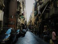 Narrow dark street with cobblestones pavement of historical Naples downtown with typical Mediterranean apartment houses with tiny balconies and wooden/Photo by Ewelina Lepionko