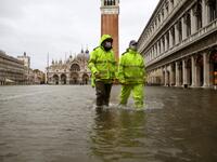 Men wearing waterproof gear walk across a flooded St. Mark's Square on December 8, 2020 following a high tide "Alta Acqua" event following heavy rains and strong winds, and the mobile gates of the MOSE Experimental Electromechanical Module that protects the city of Venice from floods, were not lifted. ANDREA PATTARO / AFP
