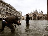 People talk photos in the middle of a flooded St. Mark's Square on December 8, 2020 in Venice following a high tide "Alta Acqua" event following heavy rains and strong winds, and the mobile gates of the MOSE Experimental Electromechanical Module that protects the city of Venice from floods, were not lifted ANDREA PATTARO / AFP
