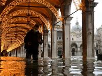 A man walks across an arcade by a flooded St. Mark's Square on December 8, 2020 in Venice following a high tide "Alta Acqua" event following heavy rains and strong winds, and the mobile gates of the MOSE Experimental Electromechanical Module that protects the city of Venice from floods, were not lifted ANDREA PATTARO / AFP