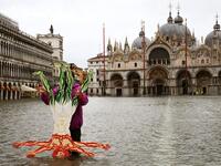 A view shows a flooded St. Mark's Square as a man poses for a photo by a cardboard cutout of the Vitruvian Man, on December 8, 2020 following a high tide "Alta Acqua" event following heavy rains and strong winds, and the mobile gates of the MOSE Experimental Electromechanical Module that protects the city of Venice from floods, were not lifted. ANDREA PATTARO / AFP