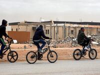 Youths play table football (foosball) outside by abandoned buildings, with graffiti nearby reading in Arabic "this zone has been cleared of the remains of war", in the city of Tawergha, some 200 kilometres (125 miles) east of Libya's capital close to the port city of Misrata, on December 12, 2020. When Libyan dictator Moamer Kadhafi was toppled, people took revenge on those they saw as his supporters -- including the entire town of Tawergha, whose 40,000 residents were forced to flee. Now, almost a decade l