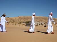 Former inhabitants of Wadi al-Murr, walk near abandoned houses in the Omani village, about 400 kms (250 miles) southwest of the capital Muscat, on December 31, 2020. Encroaching desert sands have left little evidence that Wadi al-Murr ever existed, but former inhabitants, while resigned to its destruction, are trying to preserve its memory. MOHAMMED MAHJOUB / AFP