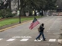 A man walks with a U.S. flag on the Washington State Capitol campus on January 20, 2021 in Olympia, United States. One Donald Trump protester held a sign at an otherwise quiet capitol campus on Presidential Inauguration Day today. David Ryder/Getty Images/AFP