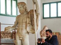 A man uses a phone to take a picture of a Roman statue of Jupiter 