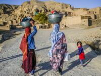 In this picture taken on October 3, 2021, Hazara ethnic women walk with their laundry to their village near the cliffs pockmarked by caves where people still live as they did centuries ago in Bamiyan. 