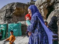 In this picture taken on October 3, 2021, a Hazara ethnic woman with a baby walks in front of her cave on a cliff pockmarked by caves where people still live as they did centuries ago in Bamiyan. 