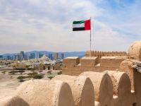 علم الإمارات العربية المتحدة يرفرف فوق قلعة الفجيرة مع أفق المدينة في الخلفية