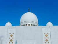 واجهة مسجد بقباب بيضاء بارزة تحت سماء زرقاء صافية، في صورة تعبيرية عن دور العبادة الإسلامية.