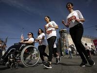 Participants push another in a wheelchair as they run along Israel's controversial separation barrier, which divides the West Bank from Jerusalem, in the biblical town of Bethlehem during the 6th International Palestine Marathon on Mar. 23, 2018. 
(Musa AL SHAER / AFP)