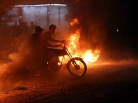 Demonstrators use a scooter to drive through burning tyres during an ongoing protest against unemployment and high cost of living in the southern Iraqi city of Basra during the night of July 12, 2018. (AFP/Haidar Mohammad Ali)

