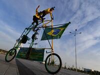 Brazilian football fans Elias de Souza and his son Elias de Souza junior perform acrobatics as they ride their homemade 3 metre-high tandem bicycle near Rostov Arena in Rostov-on-Don on June 16, 2018, on the eve of the match between Brazil and Switzerland during the Russia 2018 FIFA World Cup football tournament. 
JOE KLAMAR / AFP
