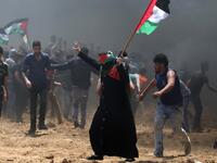 A Palestinian woman waves her national flag during clashes with Israeli forces near the border between Israel and the Gaza Strip, east of Jabalia on May 14, 2018, as Palestinians protest over the inauguration of the US embassy following its controversial move to Jerusalem. MOHAMMED ABED / AFP