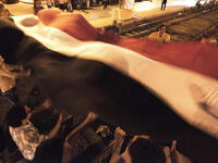 Opponents of the Egyptian president wave a giant national flag outside the presidential palace (AFP)