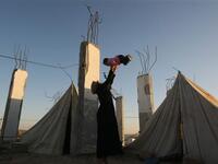 A displaced Palestinian woman carries her child outside their tent, in the Ezbet Abed Rabbo area, that was heavily destroyed during Israel's 22-day offensive on the Gaza Strip.