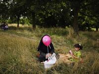A woman and girl sit in the shade in Burgess Park during an Eid celebration fun fair in London, England. (GETTY)