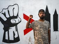 Sudanese graffiti artist Amir Saleh poses in front of a recently painted mural made by his team during a protest near the army headquarters in the capital Khartoum (AFP)