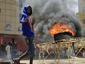 A Sudanese protester gestures as he walks past a burning tyre near Khartoum's army headquarters on June 3, 2019 after security forces broke up a weeks-long sit-in. (AFP)