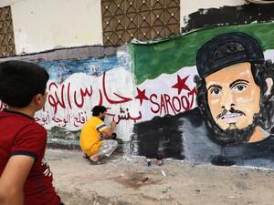 A child watches as a local artist works on a mural painting showing the late Syrian rebel fighter Abdel-Basset al-Sarout in the town of Binnish in the jihadist-held northern Idlib province on June 8, 2019. (OMAR HAJ KADOUR / AFP)