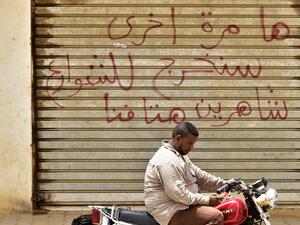 A Sudanese man sits on a motorbike in front of a closed photo studio in Khartoum on June 9, 2019. Arabic writing on the shutters of the closed shop reads: "Another time, we shall take to the streets, crying out our demands loudly." (AFP/ File Photo)