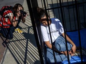 A photographer takes a picture of a teenager sitting in a cage during a protest of international labor groups, civil society and students against the policy of migrant family separation along the US-Mexico border on June 17, 2019 in front of the United Nations offices in Geneva. (FABRICE COFFRINI / AFP)