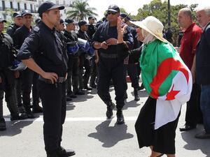 An Algerian protester wrapped with a national flag confronts riot police during the weekly Friday demonstration in the capital Algiers on June 21, 2019. (AFP)