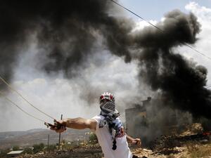 Smoke billows from burning tires as a Palestinian protester uses a slingshot to hurl stones at Israeli troops, during clashes following a weekly protest against the expropriation of Palestinian land by Israel, in the village of Kfar Qaddum near the Jewish settlement of Qadumim (Kedumim), in the Israeli-occupied West Bank on July 19, 2019.  JAAFAR ASHTIYEH / AFP