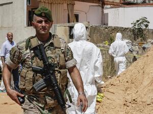 A Lebanese army soldier walks past military intelligence forensic investigators inspecting the scene where two drones came down in the vicinity of a media centre of the Shiite Hezbollah movement  (AFP)