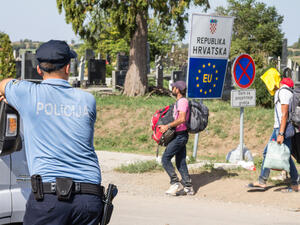 Croatian police officer looking at Refugees passing in front of the EU entrance sign on the Serbia-Croatia border crossing. (Shutterstock/ File Photo)