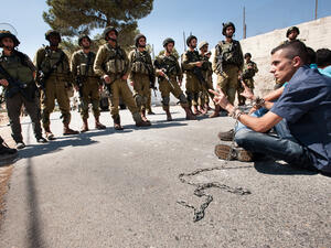 Palestinians in chains symbolizing solidarity with prisoners in Israeli jails face soldiers during a protest in Al Ma'sara, West Bank. (Shutterstock/ File Photo)