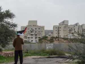 A Palestinian protester stands near the West Bank Barrier holding a flag as a form of protest in Bilin, West Bank, Palestine. (Shutterstock/ File Photo)