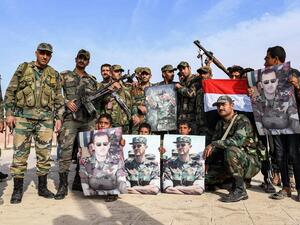 Syrian government soldiers pose for a group photo with a national flag and portraits of President Bashar al-Assad on the outskirts of the northern city of Manbij in the north of Aleppo province as government forces deploy there on October 15, 2019. (AFP/ File Photo)