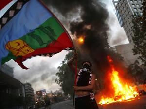 A demonstrator flutters a Mapuche indigenous flag near a bonfire in Santiago, on October 25, 2019, a week after violent protests started. Demonstrations against a hike in metro ticket prices in Chile's capital exploded into violence on October 18, unleashing widening protests over living costs and social inequality. (Pablo VERA / AFP)